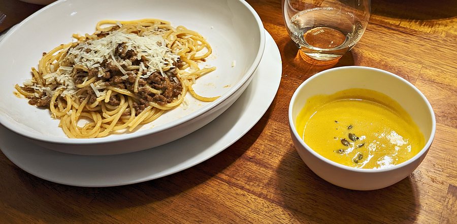 Spaghetti with ragù and parmesan beside a bowl of squash soup