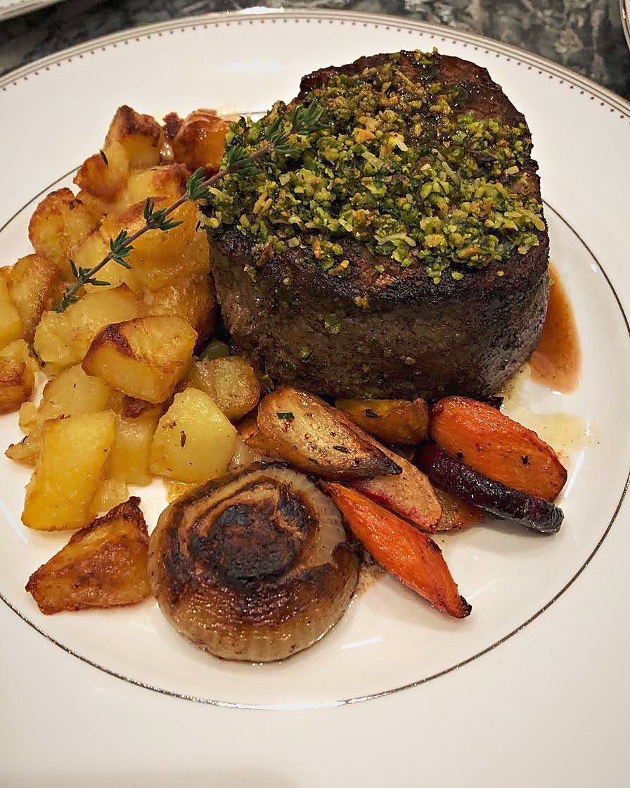 Herb and pistachio crusted filet with roast potatoes, carrots and roasted onion on a fine rimmed plate